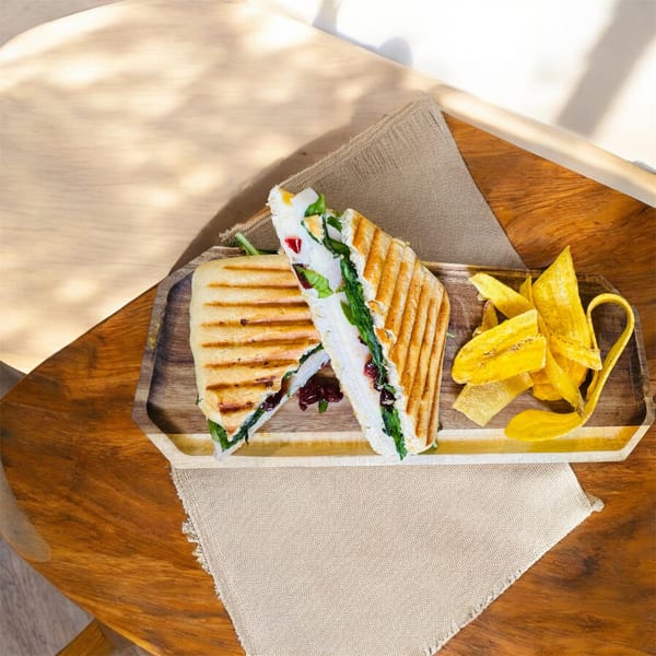 Grilled Latin-American sandwich with spinach and plantain chips on a wooden tray.