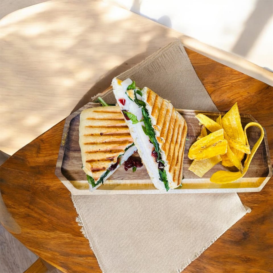 Grilled Latin-American sandwich with spinach and plantain chips on a wooden tray.