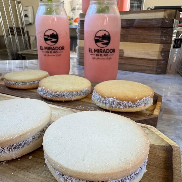 Alfajores with coconut flakes and two pink El Mirador En El Rio drinks on a wooden tray.