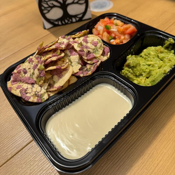 A black plastic tray with chips, salsa, guacamole, and a creamy dip on a wooden table.