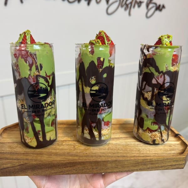Three El Mirador En El Rio desserts in clear cups with green and chocolate drizzle, strawberries, and nuts.